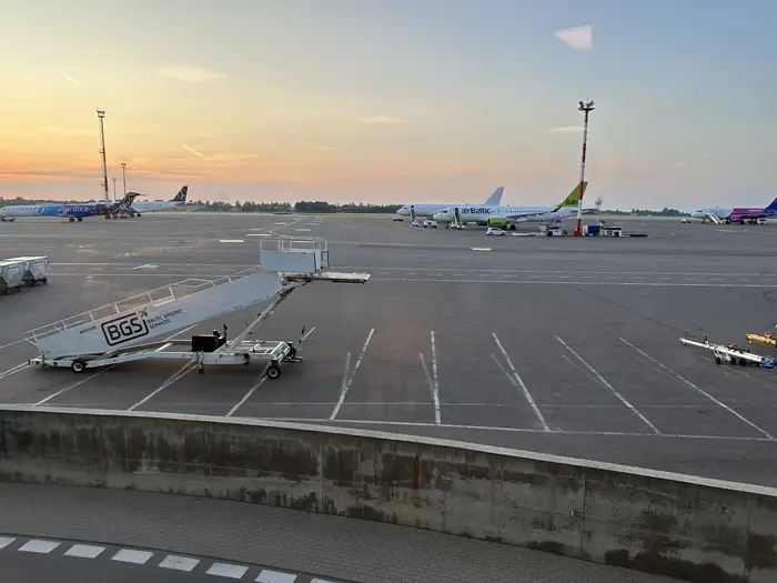 An airport apron at sunset with parked airplanes from airBaltic, Nordica, and Wizz Air, with mobile boarding stairs in the foreground.