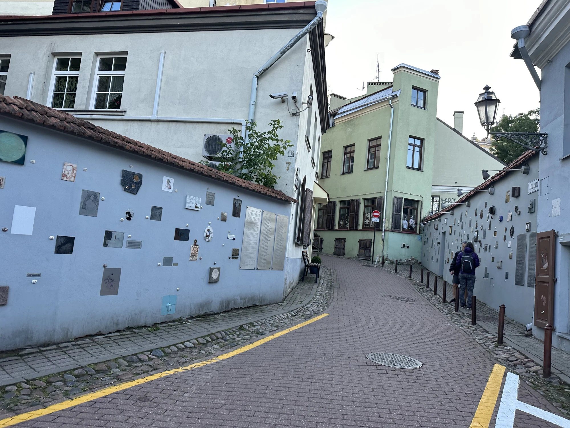 A narrow paved street curves between historic buildings, with light blue walls decorated with small artistic plaques and tiles.