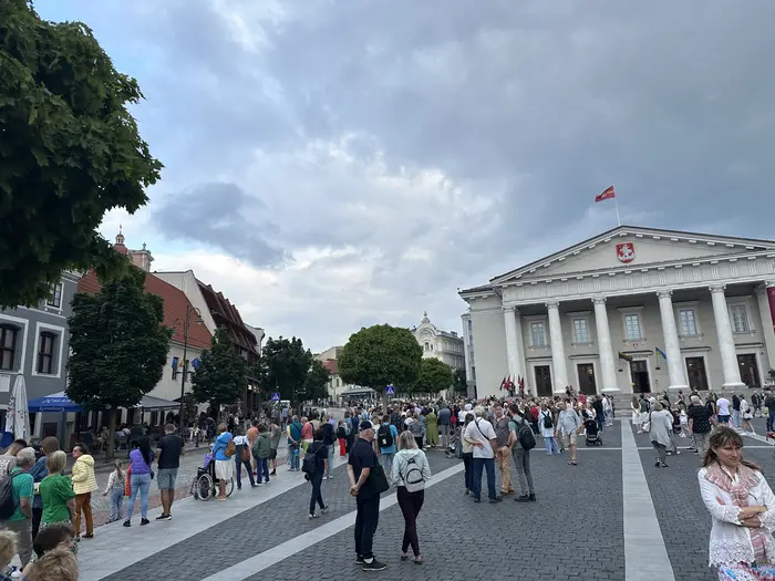 A wide shot of the neoclassical Vilnius Town Hall and the surrounding square filled with people on an overcast day.