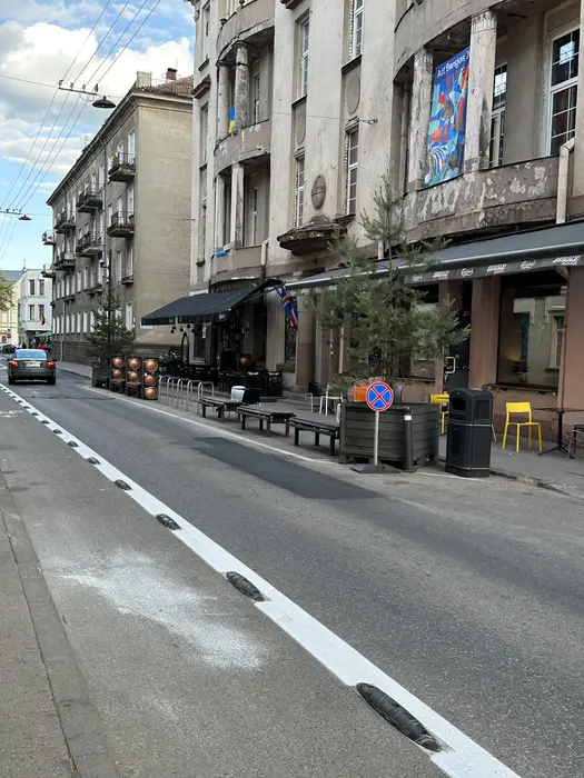 A street view of Islandijos Street in Vilnius, showing historic apartment buildings with ground-floor cafes, outdoor seating, and a bicycle lane.