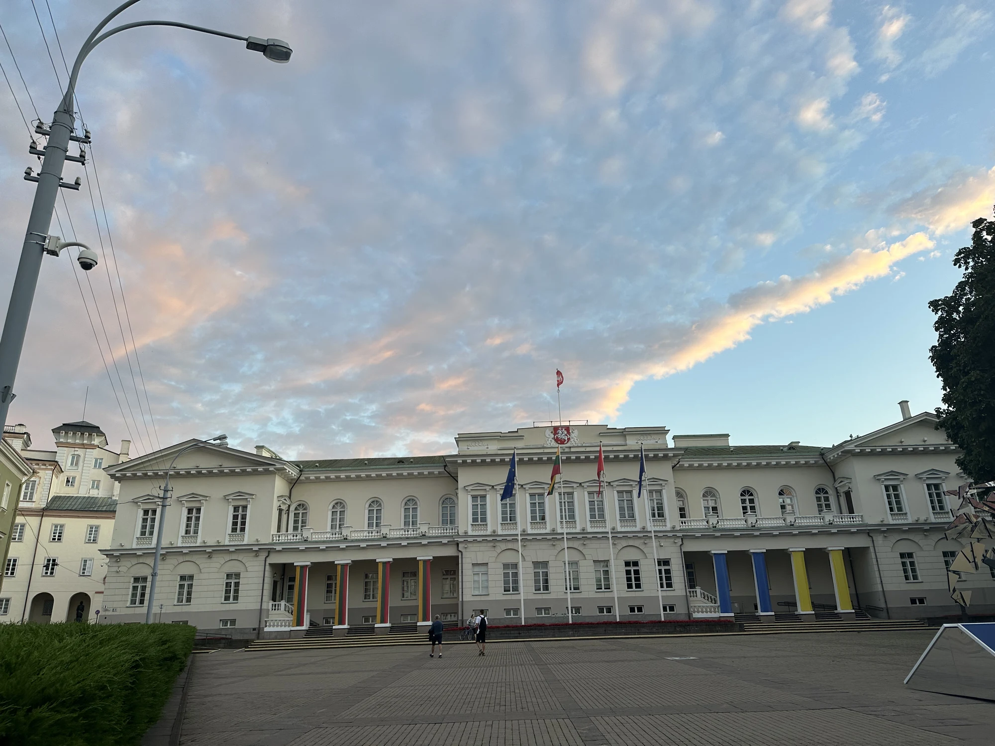 The neoclassical facade of the Presidential Palace of Lithuania in Vilnius, viewed from Daukanto Square under a sky with pink-tinged clouds.