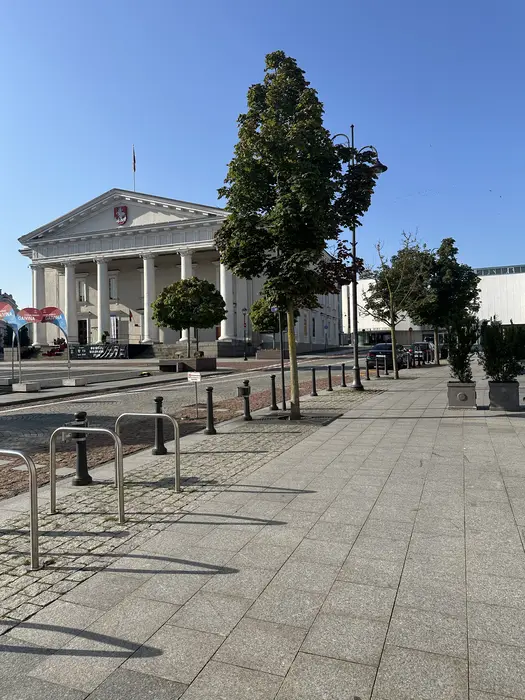 The neoclassical Vilnius Town Hall building seen from across the paved Town Hall Square on a sunny day with bike racks in the foreground.